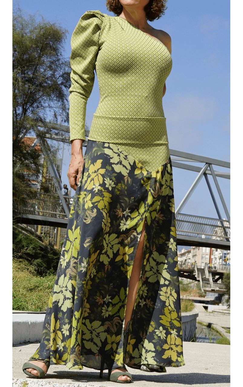 Vestido largo EMMA de EVA TYCHÉ en verde oliva, con escote asimétrico, un hombro descubierto, una manga larga, cuerpo de estampado geométrico y falda de estampado floral. / EMMA olive-green maxi dress by EVA TYCHÉ with an asymmetric neckline, one exposed shoulder, one long sleeve, a geometric-print bodice and a floral-print skirt.