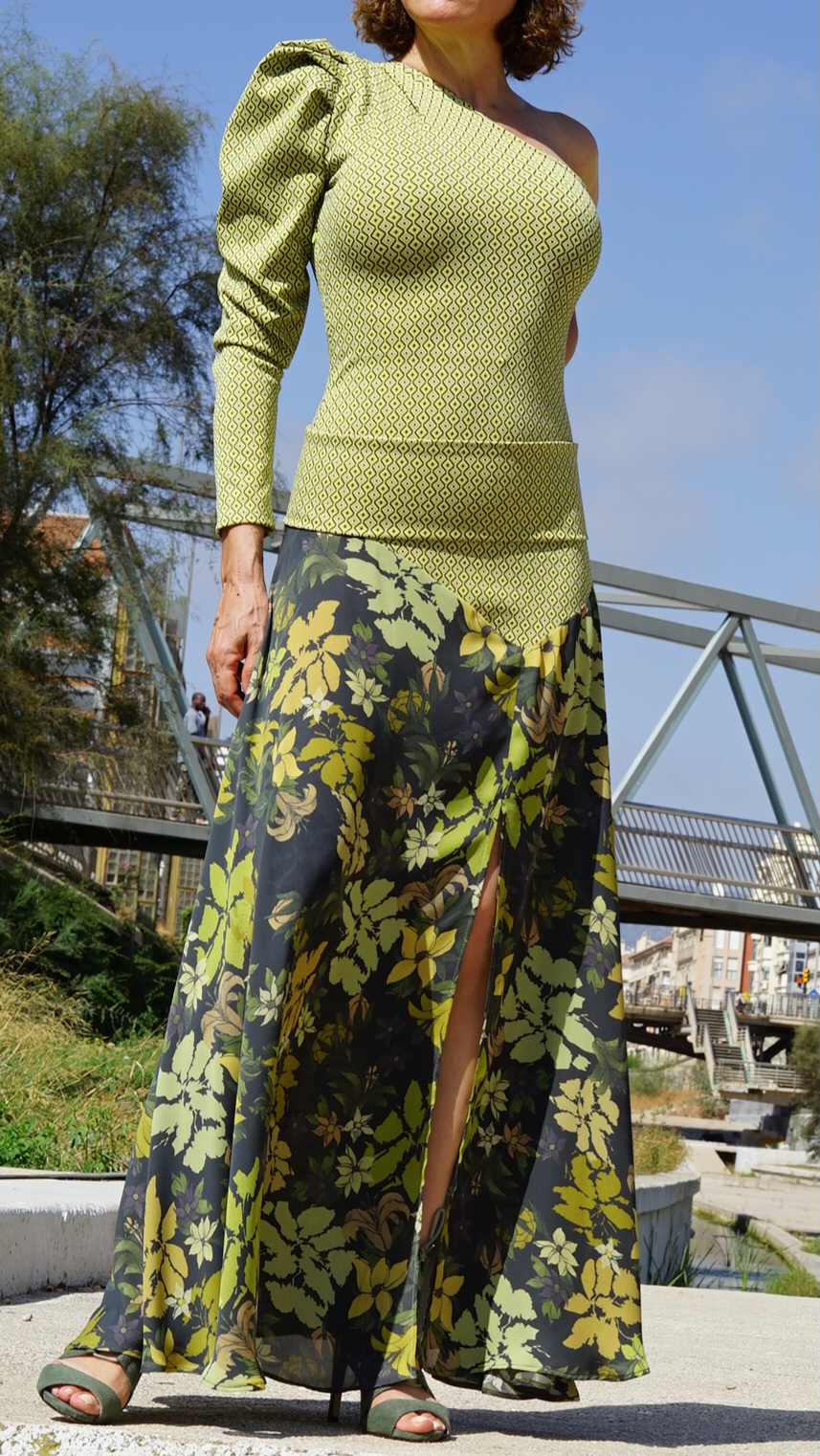 Vestido largo EMMA de EVA TYCHÉ en verde oliva, con escote asimétrico, un hombro descubierto, una manga larga, cuerpo de estampado geométrico y falda de estampado floral. / EMMA olive-green maxi dress by EVA TYCHÉ with an asymmetric neckline, one exposed shoulder, one long sleeve, a geometric-print bodice and a floral-print skirt.